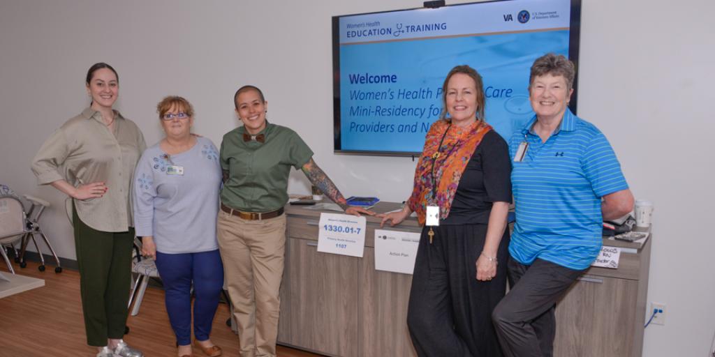 Five women stand together in front of a reception desk.
