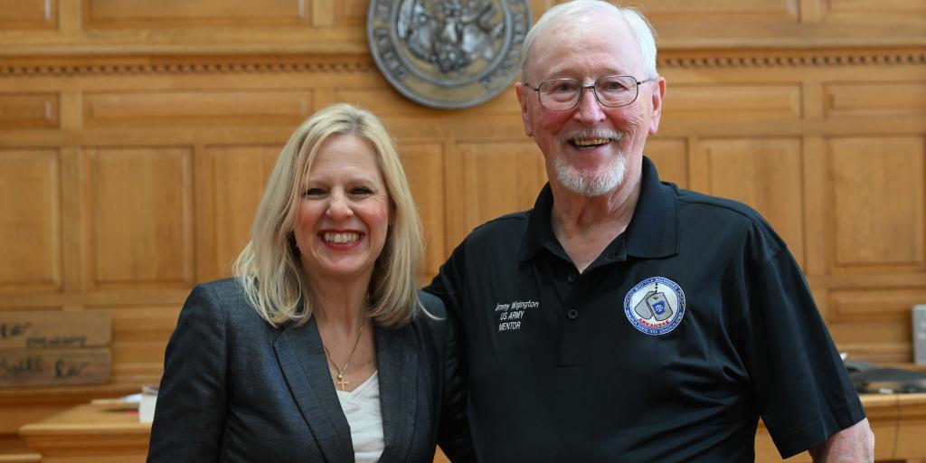 A blonde woman and an older man in a black shirt smile for a photo in a courtroom.