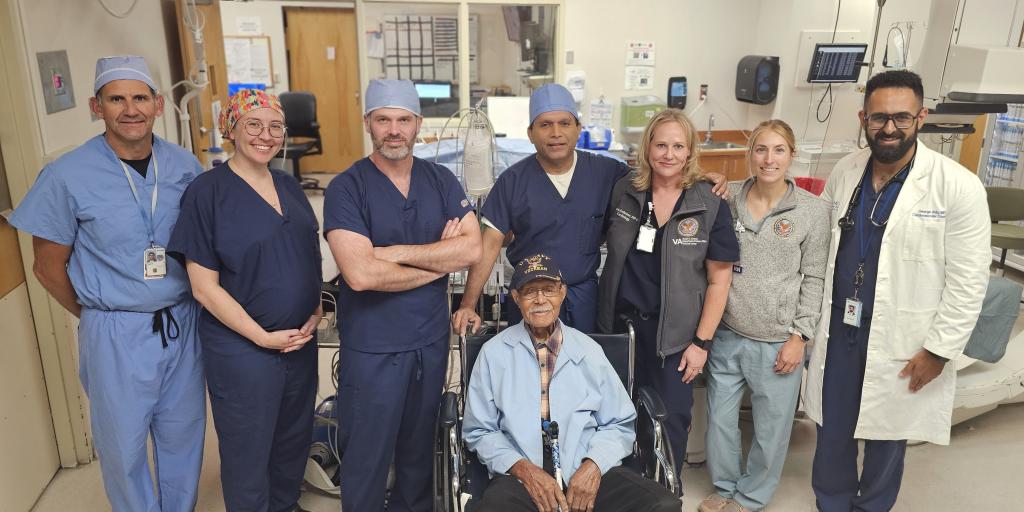 Group of hospital staff and patient smiling in hospital room.