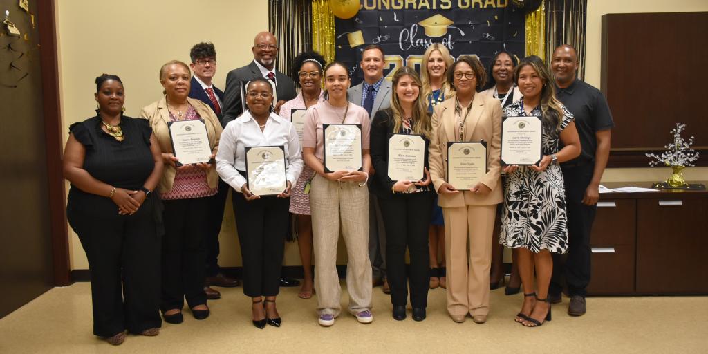 Group photo of people holding certificates in front of a banner reading "Unsung Grads".