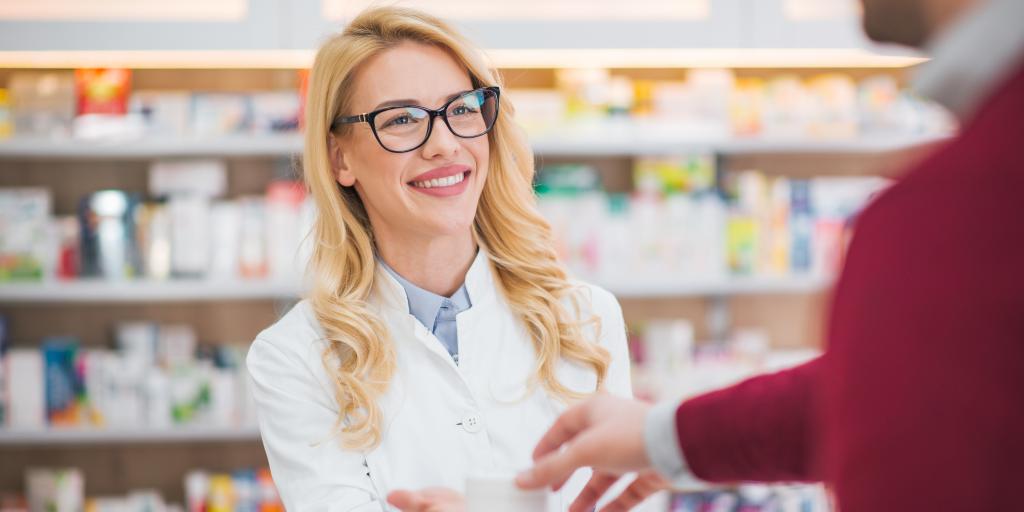 Pharmacist in white coat handing medication to customer.