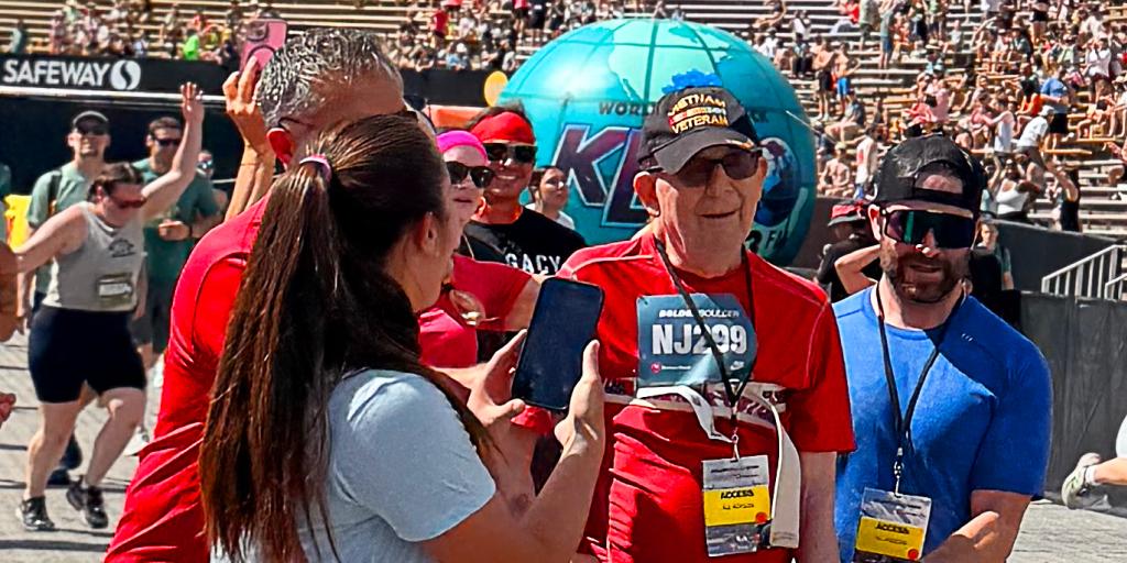 Woman taking photo of older veteran using motorized walker in front of crowd during race.