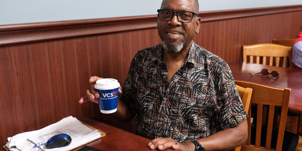 Man sitting at a desk holding a coffee cup.