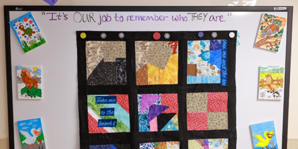 Patchwork quilt with various colors and shapes displayed on a bulletin board.
