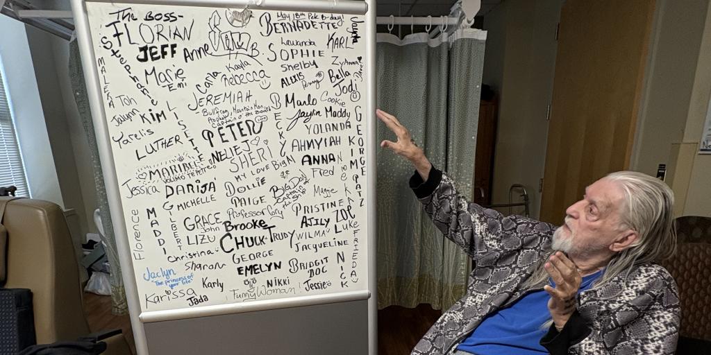 Man in wheelchair points to a whiteboard covered in writing.