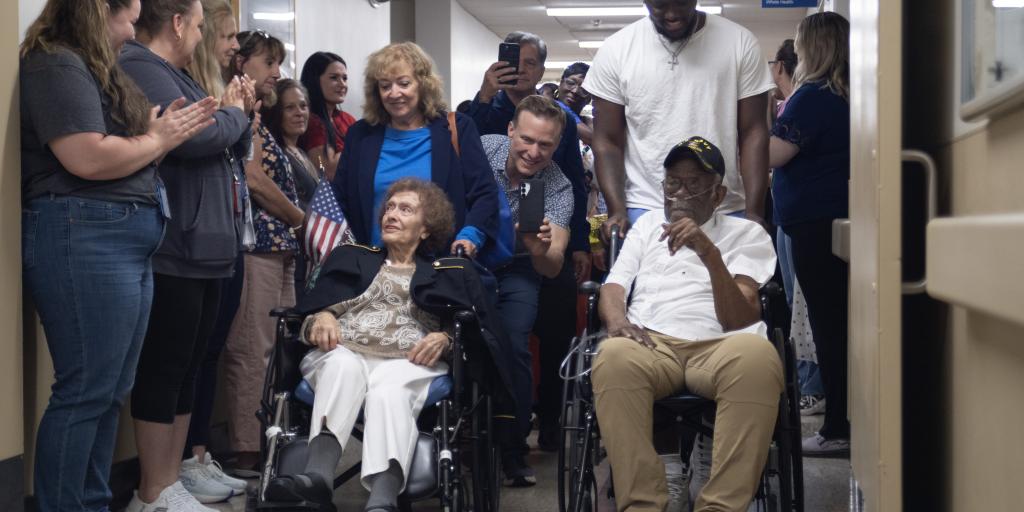 Group of people in hospital hallway with two people in wheelchairs.