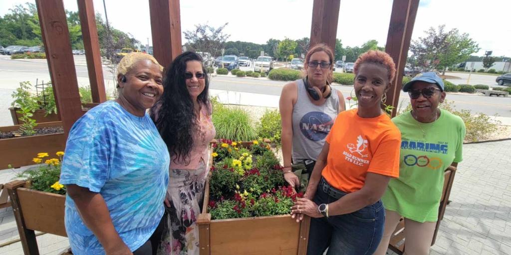 Five women stand together in front of a flower planter.