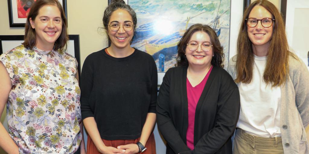 Four women in professional attire stand together in front of framed artwork.
