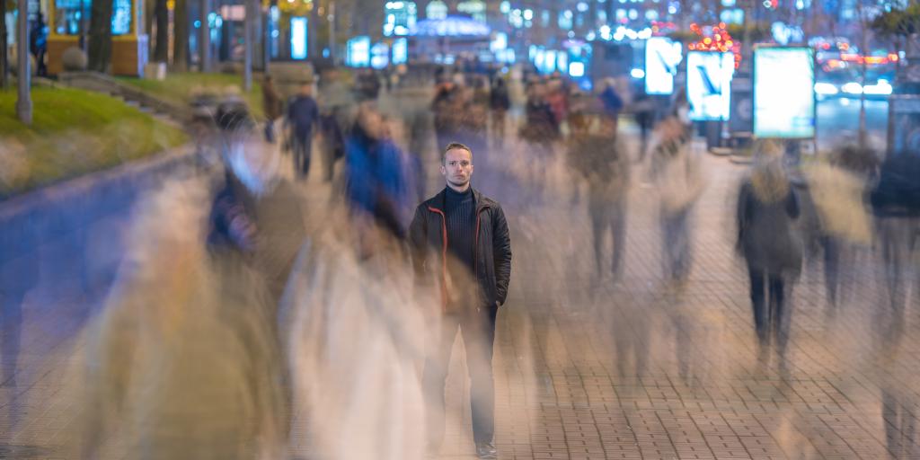 Young man walking alone on a busy, blurred city street at night.