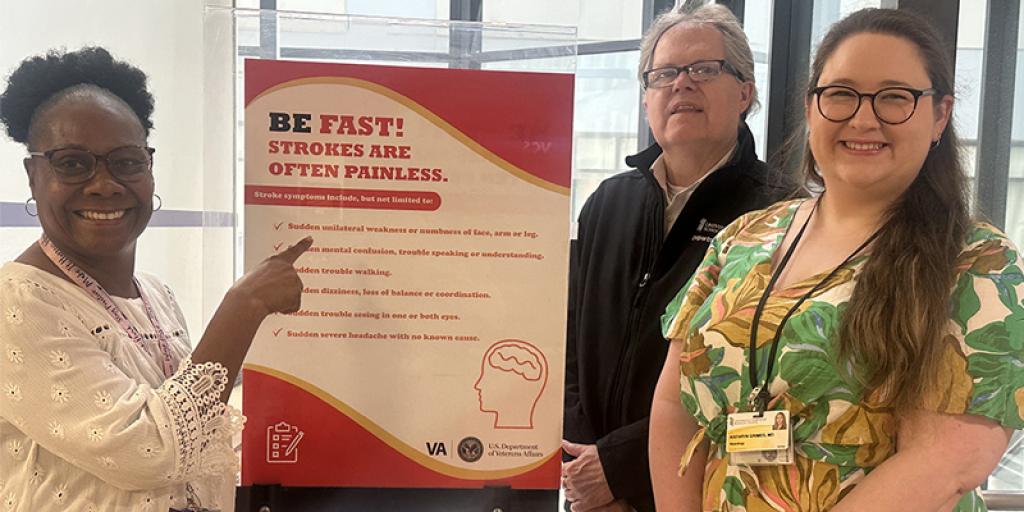 Two women and a man stand behind a poster titled "Be Fast! Know the Signs of a Stroke."