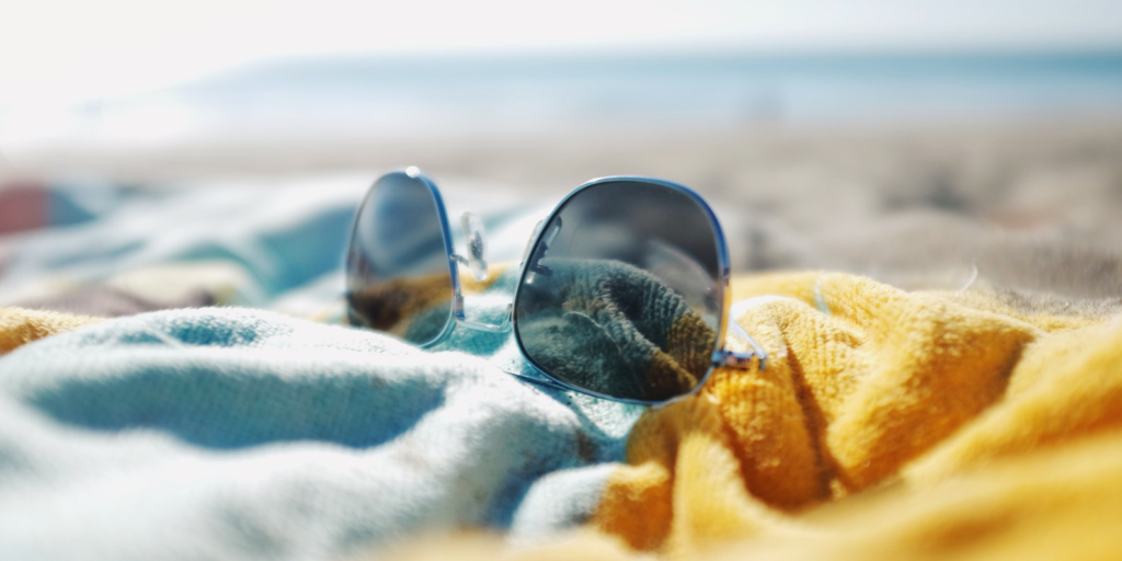 Sunglasses on blue and yellow towel at beach.