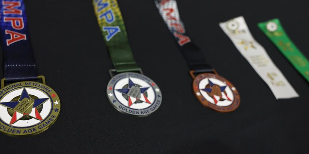 Three National Veterans Golden Age Games rest on a table with two additional award ribbons.