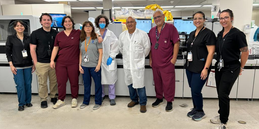 Nine people stand in a lab, smiling for a group photo.