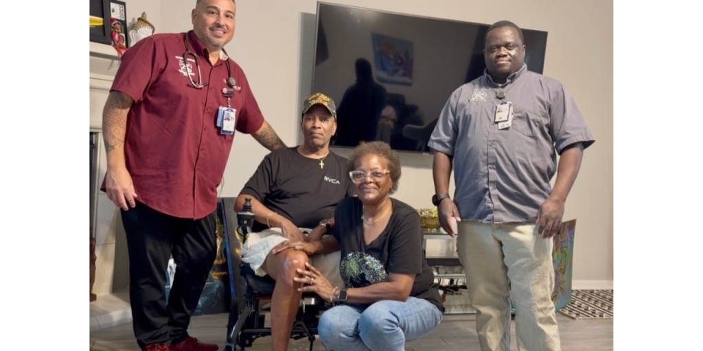 Four individuals, one in a wheelchair, pose for a photo in a living room.