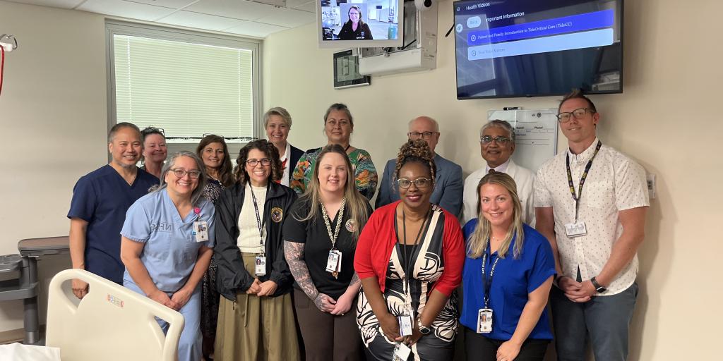 a group of people smiling for a photo underneath the new tele critical care screen in an ICU room 