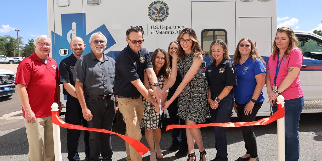 Group of people cutting a ribbon in front of a white ambulance.