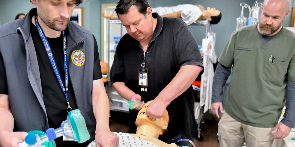 Three men practicing CPR on a dummy in a hospital room.