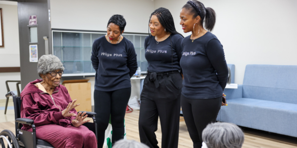 Three women in black shirts standing, one woman in wheelchair talking.