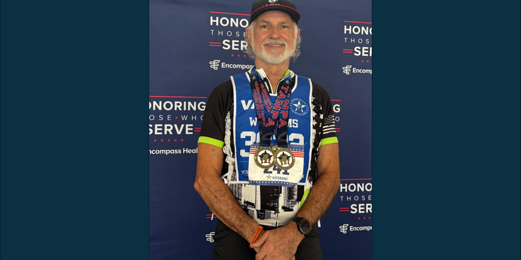A man with medals and a bib stands in front of a blue backdrop.