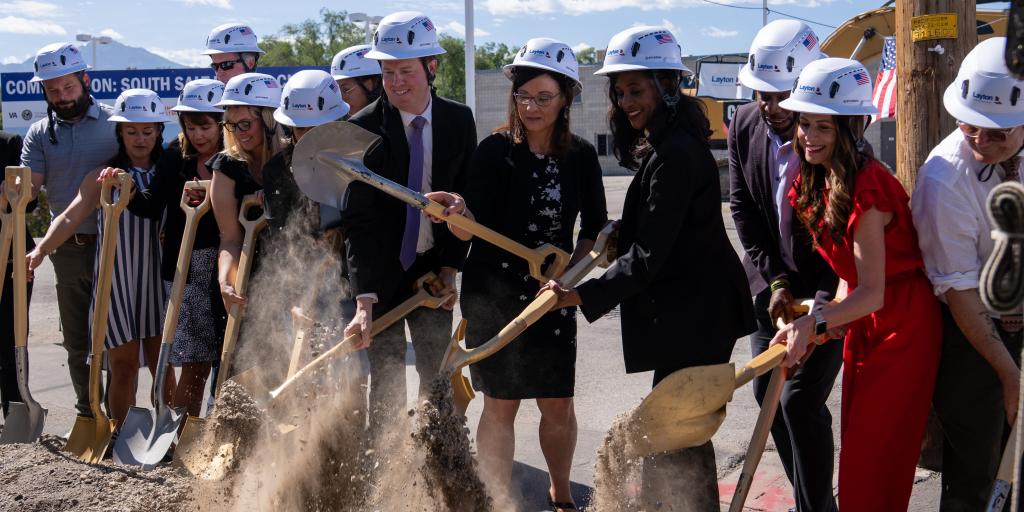 Group of people in formal wear and hard hats breaking ground with shovels.