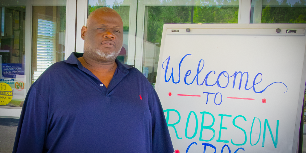Man standing outside building next to "Welcome to Robeson CBOC" sign.