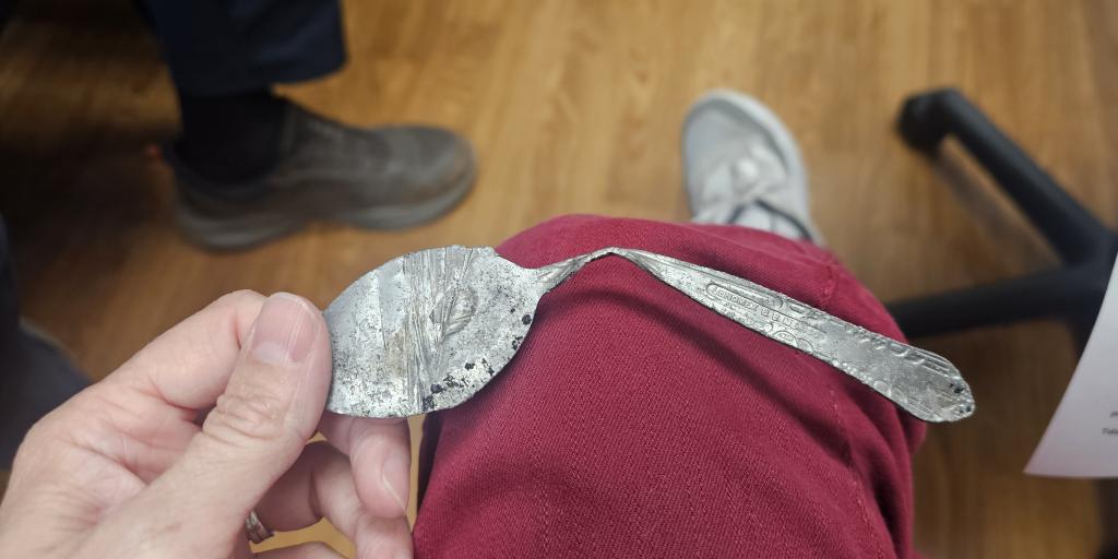Hand holding a silver spoon bent at a 90-degree angle.