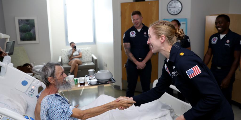 A military servicewoman shakes hands with a patient in a hospital bed.