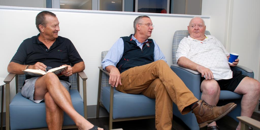Three men sitting in chairs, talking and smiling.