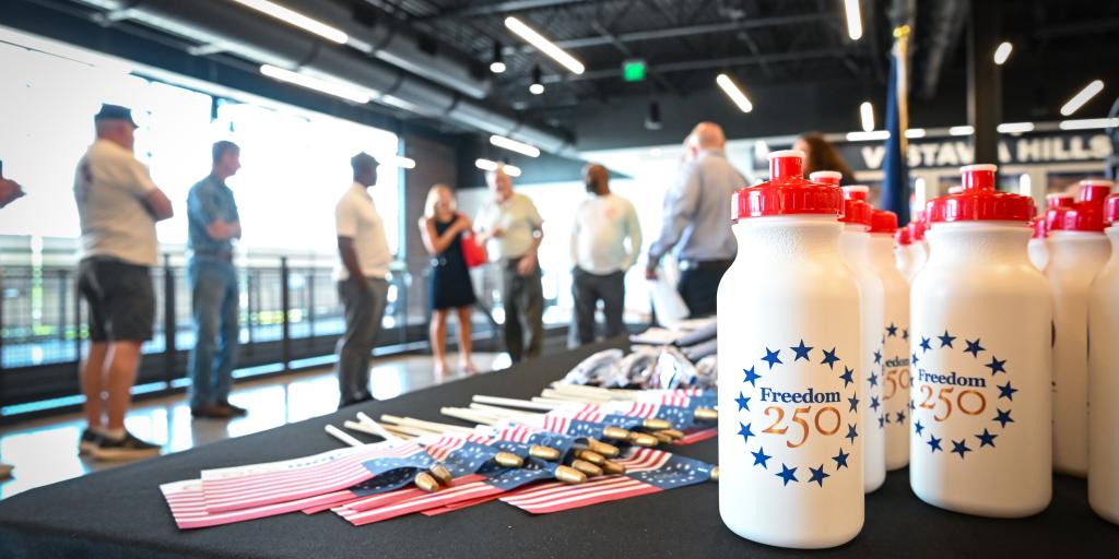 Group of people waiting in line at a table with "Freedom 250" bottles.