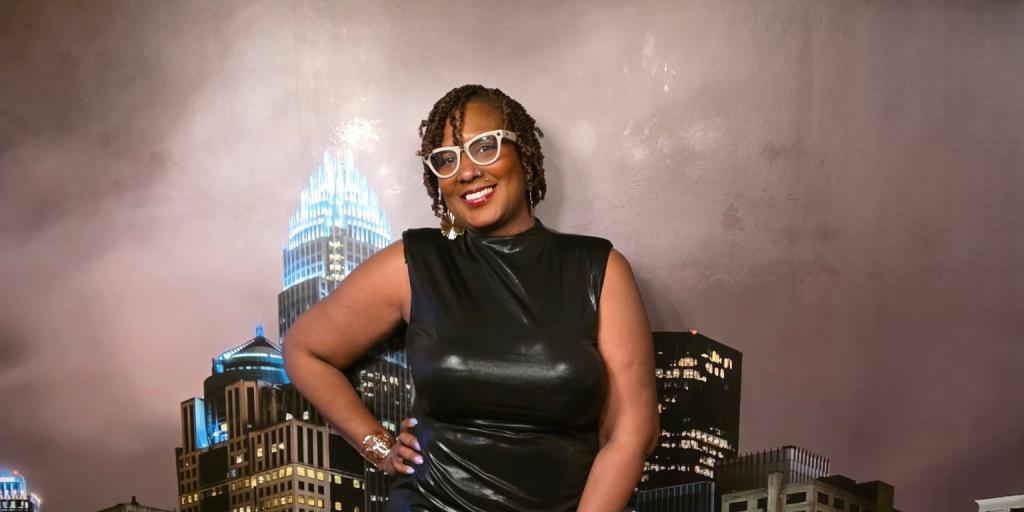 Woman in black dress stands smiling before large city skyline photo.