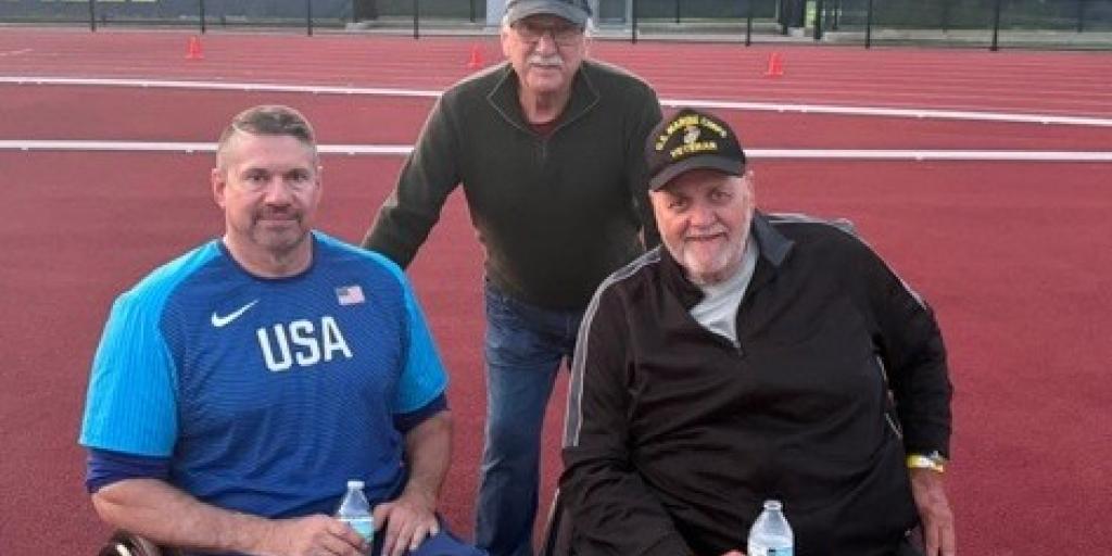 Three men, two in wheelchairs, on a track field.