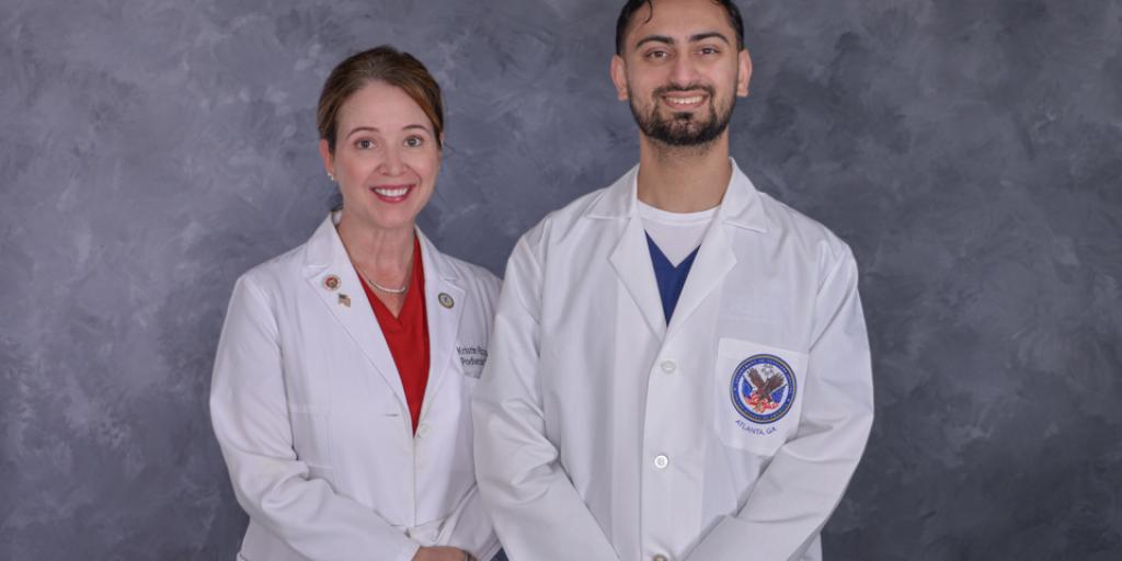 Two medical professionals in white lab coats standing together against a gray background.