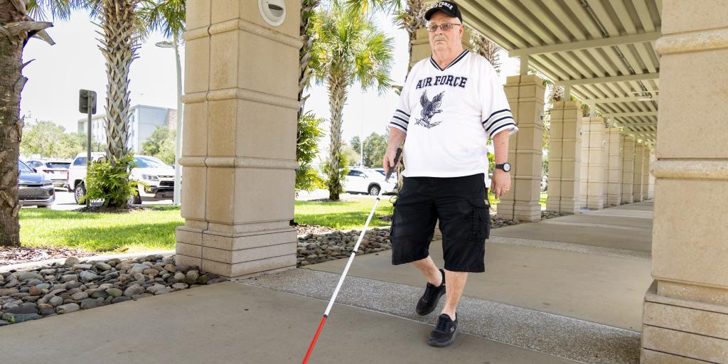 Man using a white cane with red tip to navigate.