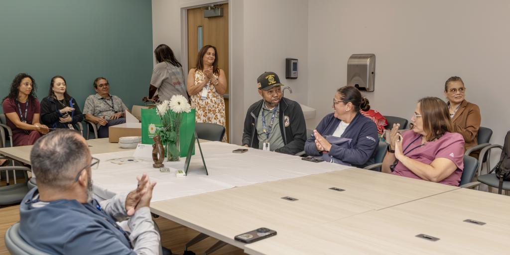 Group of people in a conference room with long tables, applauding.