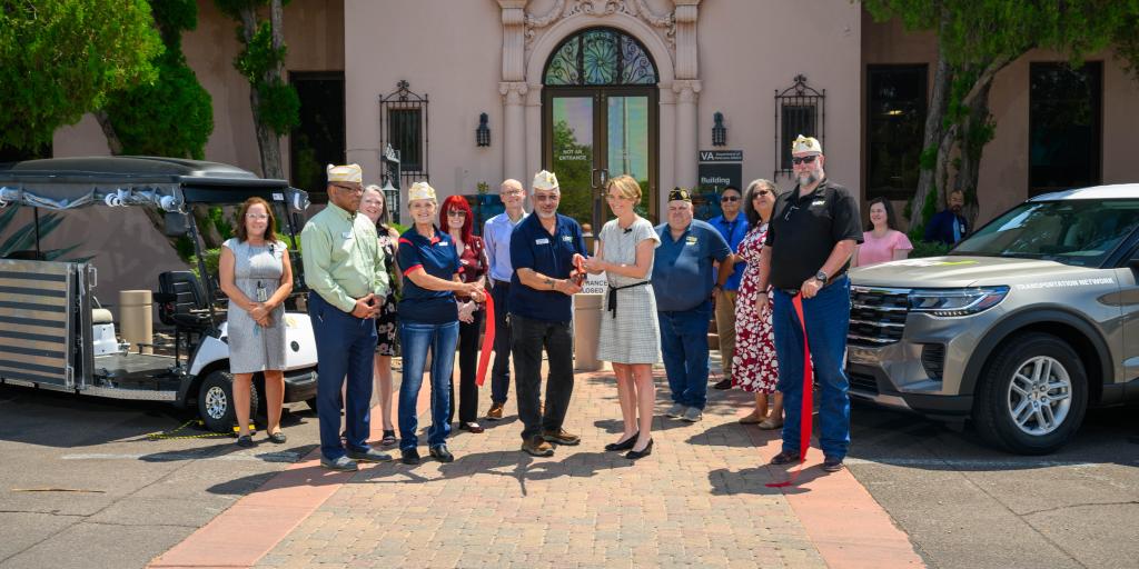Group of people cutting ribbon in front of a building.