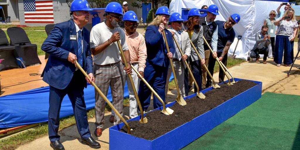 Group of people wearing hard hats break ground with shovels.