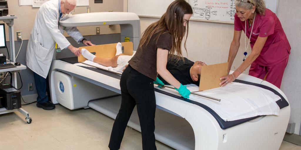 Three medical professionals assisting a patient on a scanning bed in a hospital room.