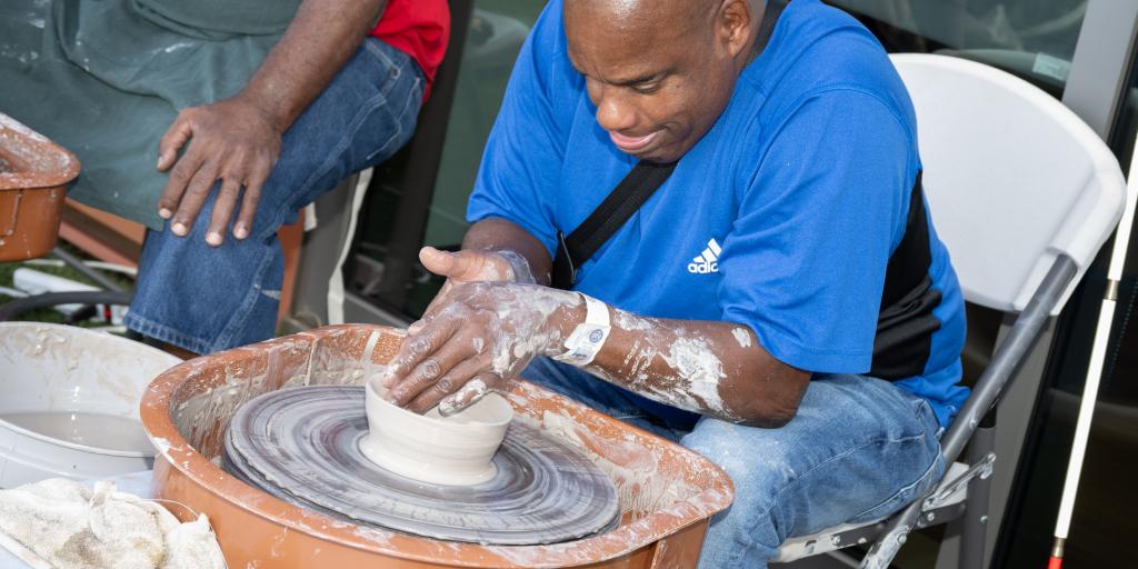Man in blue shirt and jeans crafting pottery on a potter's wheel.