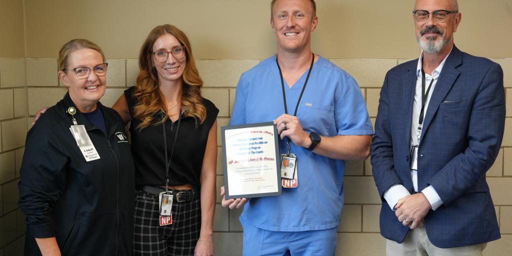 Four people stand together holding a certificate. Two wear scrubs.