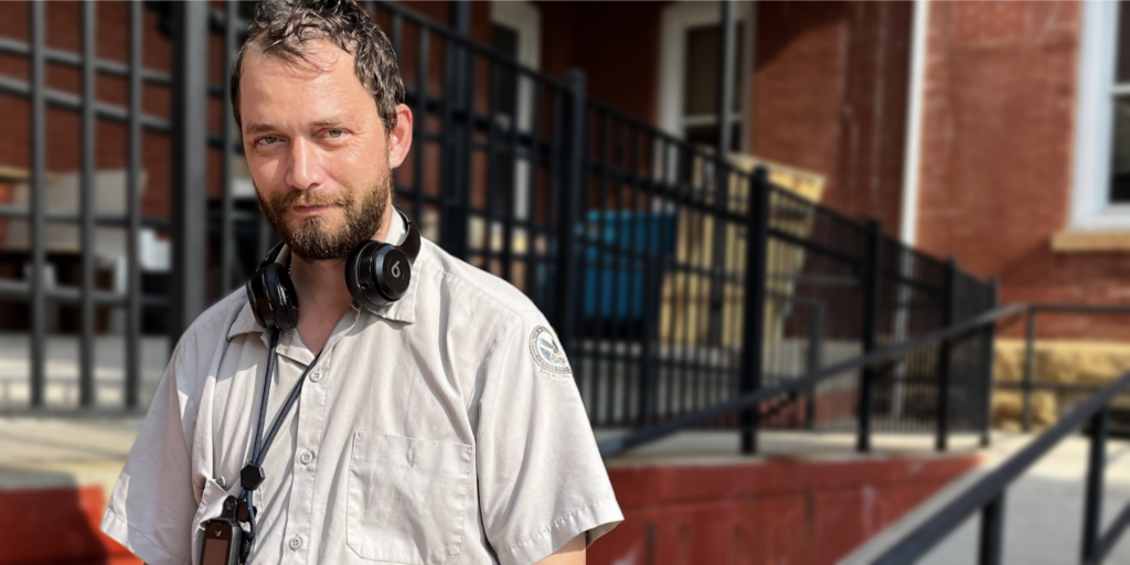 Man with headphones around his neck standing outside a brick building.