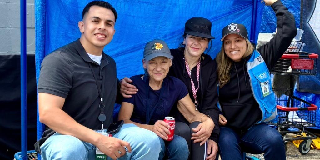 Four people sitting under a blue tent, smiling.