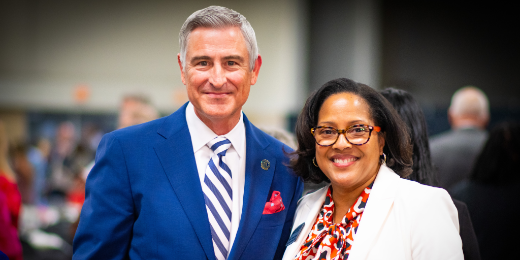 A smiling man and woman in formal attire pose for a photo at an event.