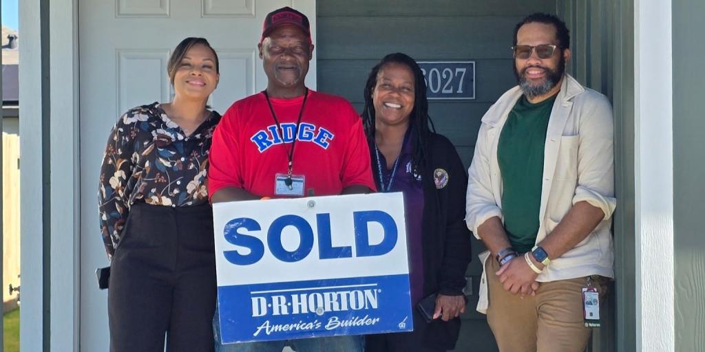 Four people stand by a door holding a "SOLD" sign.