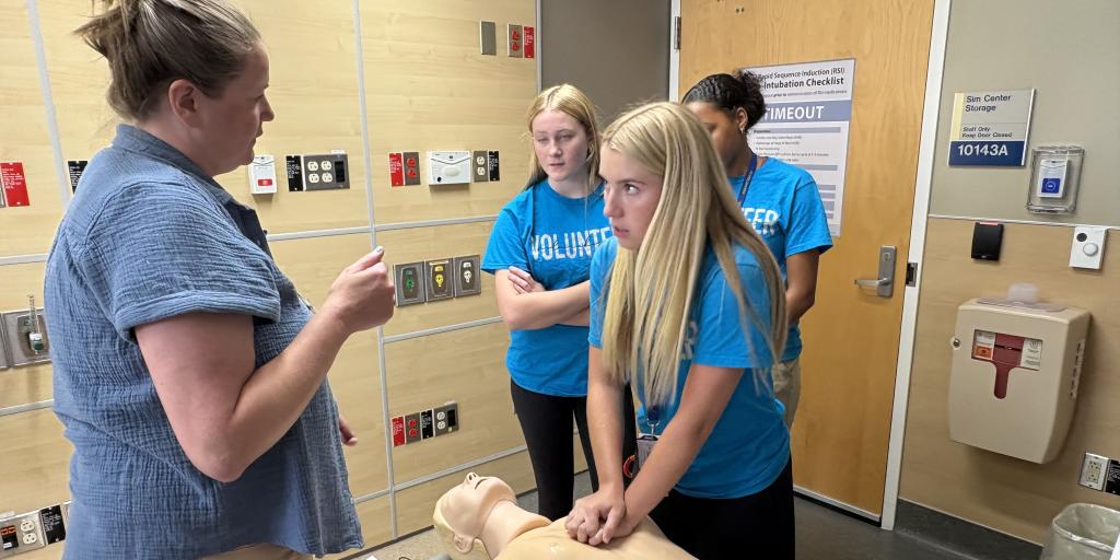 Group of four women in blue shirts working on CPR dummy.