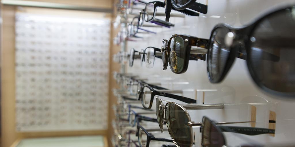 Many sunglasses and glasses displayed on a white wall in an optics store.