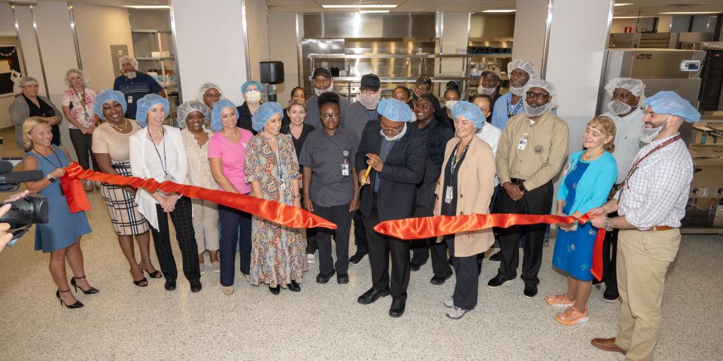 Group of people in hair nets cutting red ribbon at an opening ceremony.