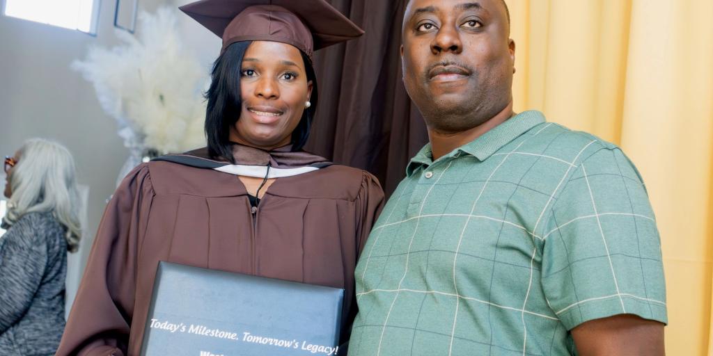 A graduate holding a diploma next to a man, both smiling.