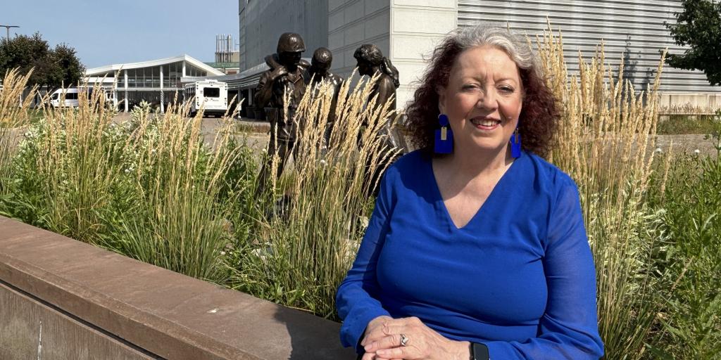 Woman in blue shirt and blue earrings sitting on a brown ledge.