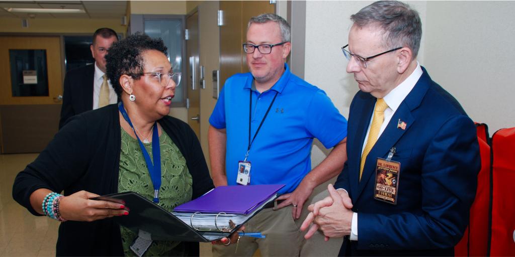 Two men and a woman discuss documents in a VA hospital hallway.