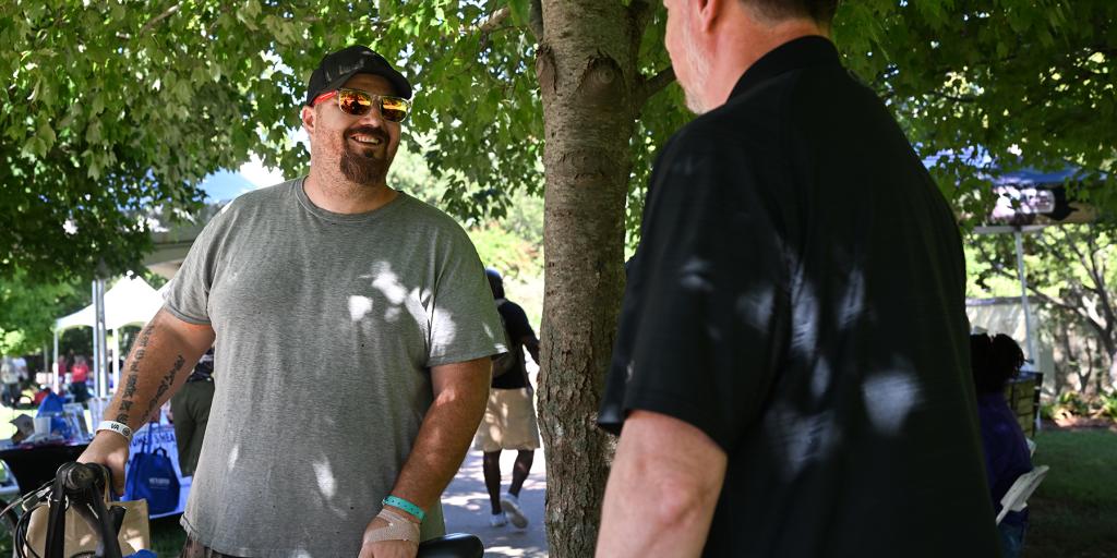 Two men chat near a tree and a bicycle.